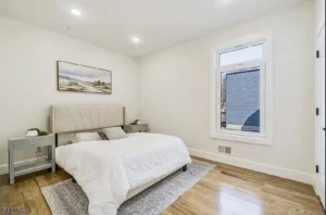 Staged primary bedroom in a vacant New Jersey home with neutral bedding, nightstands, wall art, and natural light for listing photos.
