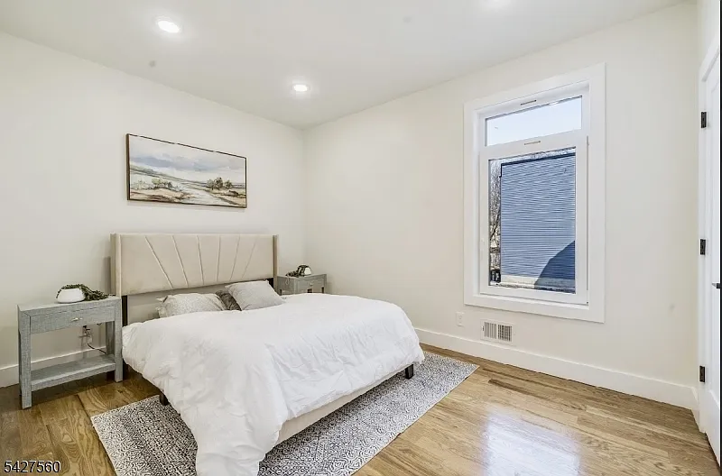 Staged primary bedroom in a vacant New Jersey home with neutral bedding, nightstands, wall art, and natural light for listing photos.