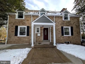 Exterior of a staged 3-bedroom renovated stone home in Abington PA with black shutters, covered front entry, walkway, and light snow.
