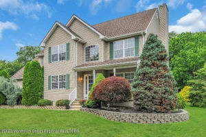 Exterior of a staged 4-bedroom Colonial home in Jackson NJ with beige siding, green shutters, manicured lawn, and mature landscaping.