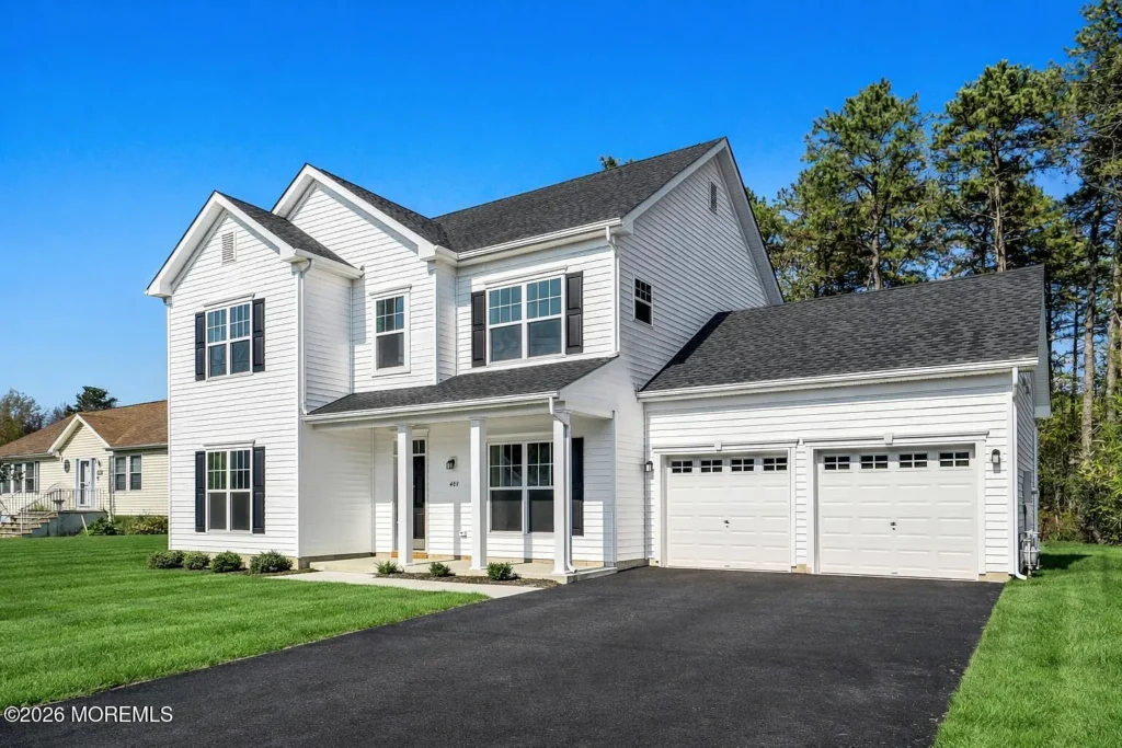 Exterior of a staged 4-bedroom Colonial home in Toms River NJ with white siding, black shutters, a paved driveway, and 2-car garage.