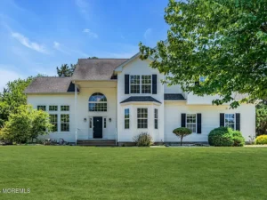 Exterior of a staged 5-bedroom Colonial home in Howell NJ with white siding, black shutters, large front lawn, and mature landscaping.
