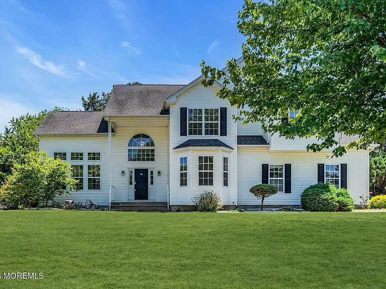 Exterior of a staged 5-bedroom Colonial home in Howell NJ with white siding, black shutters, large front lawn, and mature landscaping.