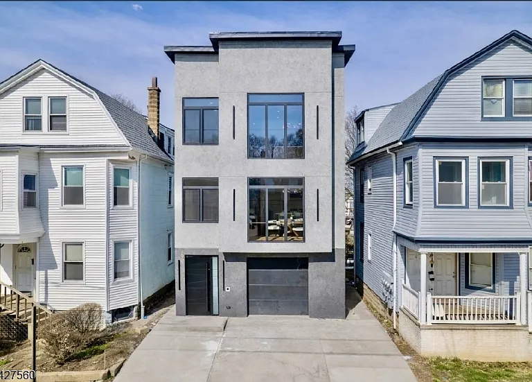Exterior of a staged 6-bedroom two-family new construction home in Irvington NJ with modern gray facade, large windows, driveway, and garage.