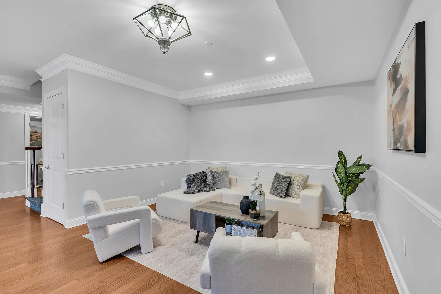 Staged Philadelphia rowhouse living room with neutral furniture, open walkway, warm wood floors, wall art, and bright lighting for listing photos.