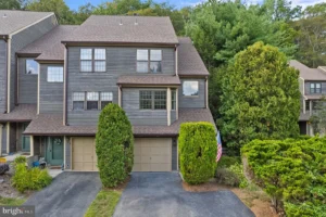 Exterior of a staged 2-bedroom townhouse in West Milford NJ with gray siding, attached garage, private driveway, and mature landscaping.