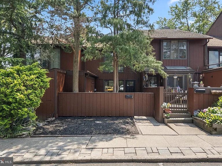 Exterior of a staged 2-bedroom contemporary townhouse in New Hope PA with brown siding, private front entry, mature trees, and landscaped walkway.