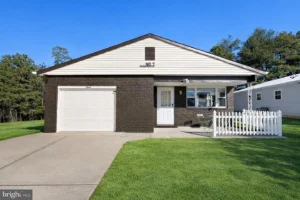 Exterior of a staged 2-bedroom ranch home in Toms River NJ with brick facade, attached garage, white picket fence, driveway, and green lawn.