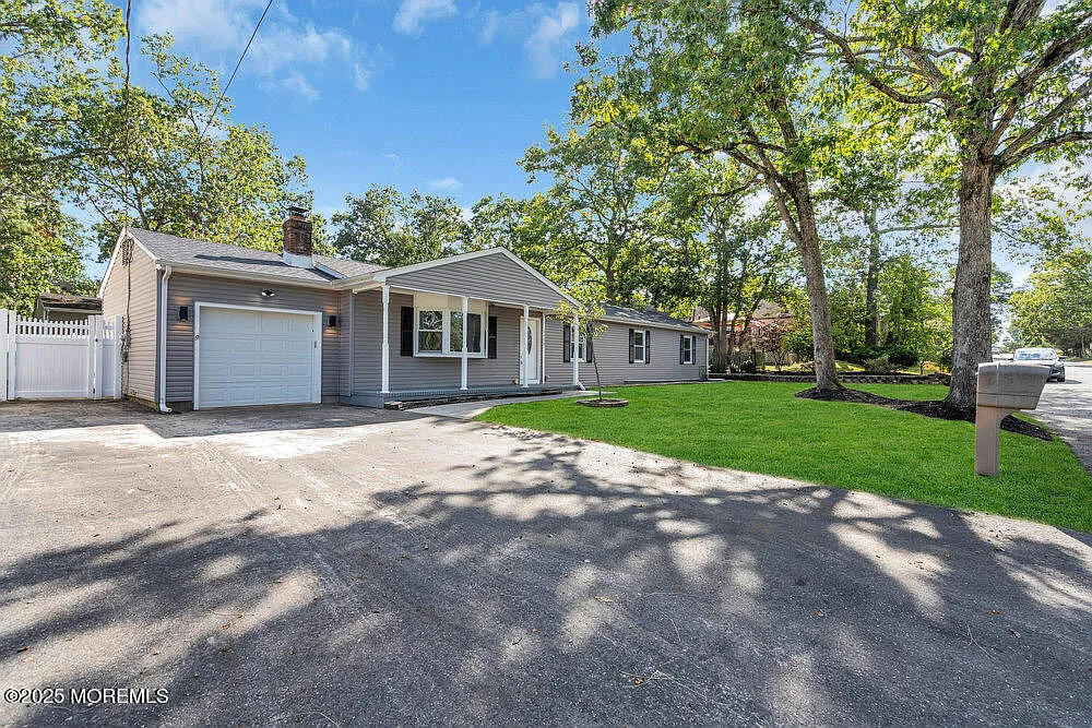 Exterior of a staged 4-bedroom Pine Lake Park ranch home in Toms River NJ with gray siding, front lawn, driveway, garage, and mature trees.