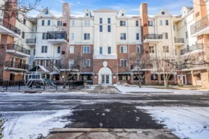 Exterior of a staged two-story condo building in Lakewood NJ with brick and cream facade, balconies, central entrance, and winter streetscape.